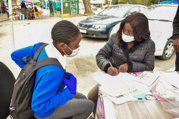A woman speaks with a young girl while writing on papers.