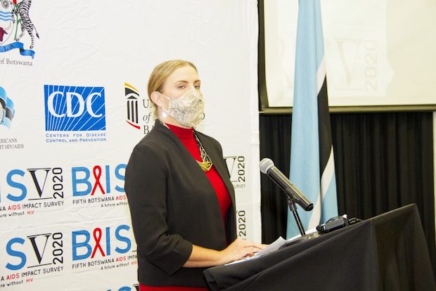 A woman wearing a face mask speaks at a lectern.