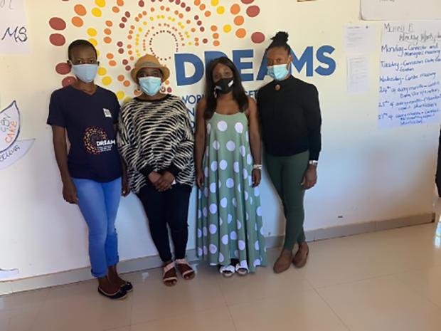 Four people wearing face masks stand in front of a DREAMS Center sign.